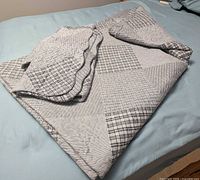 Folded grey/black patchwork quilt with matching shams on bed
