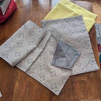 Stacked yellow tablecloths, grey patterned runner and placemats on table