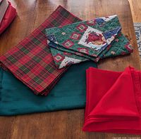 Stack of red plaid placemats, quilted Christmas runner, green tablecloth, red napkins
