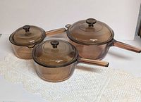 Three amber glass saucepans with lids displayed side by side