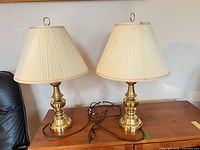 Both matching brass lamps with shades and cords on wooden surface