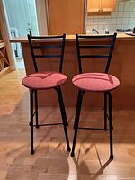 Two metal bar stools with red upholstered seats and black frames