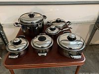 Full view of all six Carrera stainless steel pots with lids on table