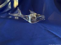 Side view of clear glass beluga figurine on blue backdrop