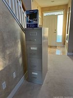 Tall 4-drawer metal filing cabinet with box of hanging folders on top