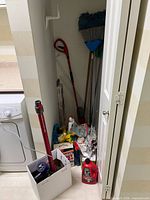 View of closet with long-handled tools, Drano bottle, box of supplies