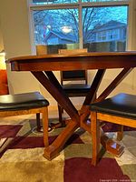 Round wooden dining table base and two chairs visible