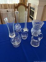 Group shot of six clear glass and crystal vases and pitcher on blue cloth