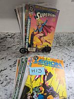 Stacked comics on stand with Supergirl #1 visible