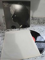 Front jacket standing, vinyl disc partly out of white inner sleeve on countertop