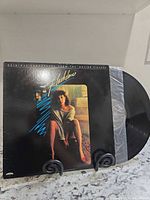 Front cover of Flashdance soundtrack LP in stand with record partially visible