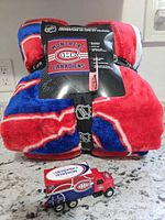 Folded Montreal Canadiens velour blanket with retail banding and tag alongside miniature Canadiens Zamboni toy