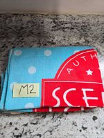 Folded Scentsy beach towel showing blue polka-dot field and red Scentsy logo panel