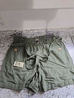Full view of olive high-rise shorts with belt and tag visible