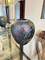 Rounded iridescent art glass vase with mottled surface on display shelf