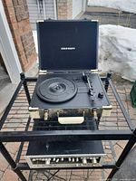 Crosley record player closed on top shelf of metal rack with Marantz amplifier below