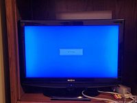 Front view of Insignia 26-inch TV powered on, shows blue no-signal screen, stand visible