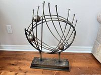 Full view of metal orbit sculpture showing spheres, curved rods and base