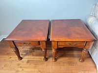 Two matching wooden side tables with drawers and fluted legs displayed side by side on hardwood floor