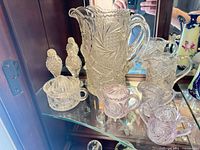 Overall view of pressed glass lot inside cabinet showing pitcher, juicer, shakers, pink cups and smaller creamer