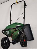 Push fertilizer spreader hanging on wall, showing wheels, frame, and hopper