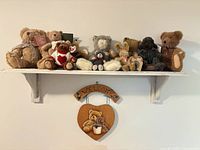 Shelf displaying nine teddy bears and wooden welcome plaque