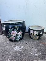 Large and small black ceramic planters side by side showing exterior floral designs