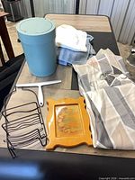 Group shot of trash can, towels, squeegee, wire rack, wall plaque, folded shower curtain with hooks