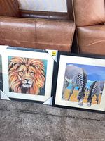 Both framed prints side by side showing lion and zebra images with black frames