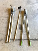 All three long-handled garden tools laid out on concrete floor