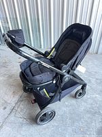 Side front view of Maxi-Cosi stroller with cup holder attached, shows wheels and basket