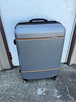 Front view of Samsonite silver hard shell suitcase showing texture, orange accent, spinner wheels