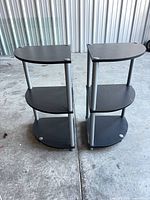 Two identical 3-tier black corner shelves side by side