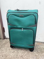 Front view teal fabric spinner suitcase with zip pockets and badge