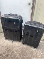Front view of both suitcases standing upright, showing glossy black hardshell exteriors and size difference