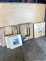 Eight natural wood picture frames standing against plywood sheet