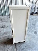 Front view of tall white cabinet with closed door and brass handle