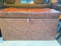 Front view of brown faux leather storage bench showing floral embossing and wear