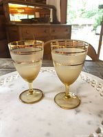 Front view of two amber frosted sherry glasses with gold banding