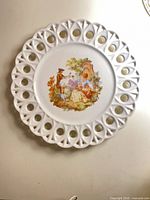 Front of white porcelain plate with pierced rim and pastoral decal