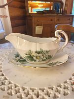 Side view of gravy boat on underplate showing floral pattern and gold trim