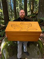 Man holding carved yellow cedar box in forest