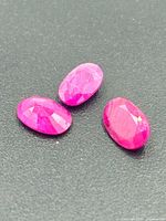 Three oval faceted ruby gemstones on dark background
