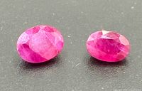 Two faceted oval ruby gemstones on dark background