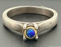 Angled view of sterling silver ring with blue opal in gold bezel