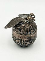 Front angled view of silver apple box showing chased floral design and leaf finial