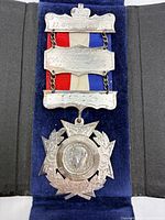 Front view of medal in open case showing crown bar, engraved plaque, date bar, ribbon and pendant
