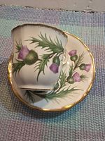 Teacup resting on saucer showing thistle design and gold trim