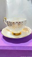 Side view of teacup on saucer showing gold lattice pattern and scalloped rim
