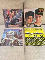 Front view of all four LP covers on sofa: City to City, Eve, Business As Usual, Bloody Tourists